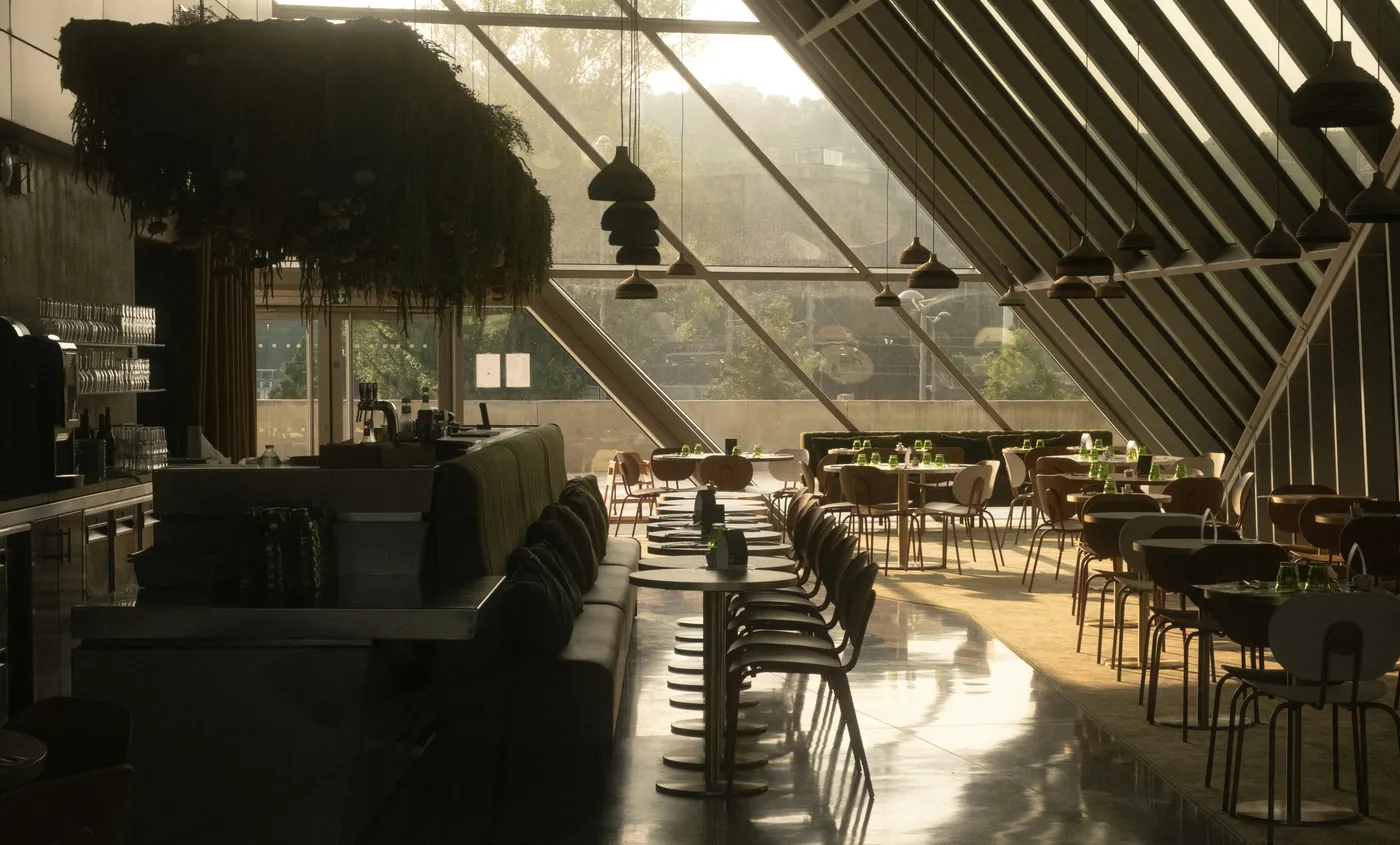 Mesas preparadas, una bancada y lámparas colgantes en un restaurante iluminado por grandes ventanales
